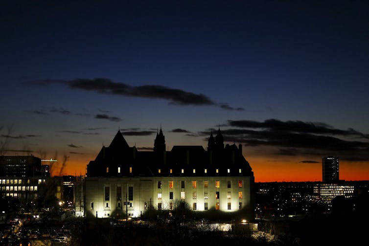 A stone building lit up against a sunset in the dusk.