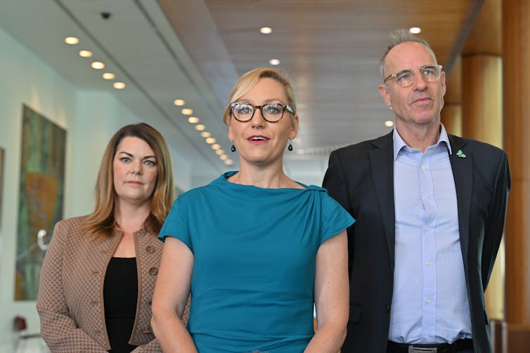 three people standing in corridor.