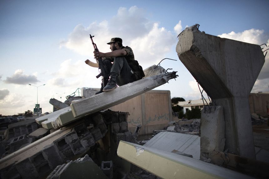 A Libyan rebel fighter sits atop the rubble of the walls which used to surround the former Libyan leader Moammar Gadhafi's compound Bab al-Aziziya in Tripoli on October 16, 2011.