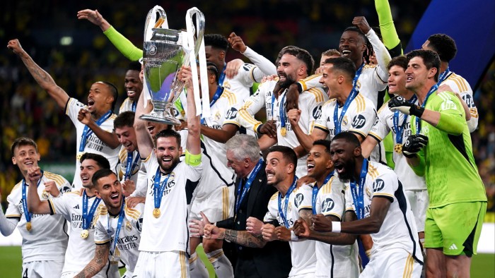 Nacho Fernandez lifts the Champions League trophy, celebrating with manager Carlo Ancelotti and jubilant Real Madrid teammates.