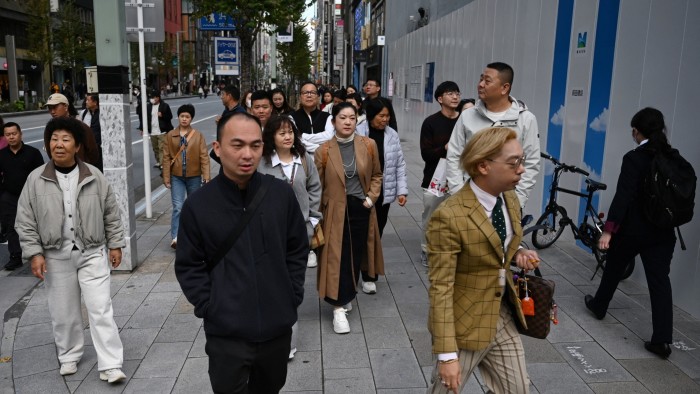 A group of Chinese tourists walks together along a busy sidewalk in Tokyo’s Ginza shopping district.