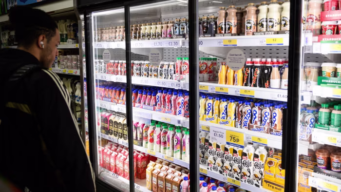 A person stands in front of a refrigerated supermarket display filled with various brands and flavours of bottled milkshakes.