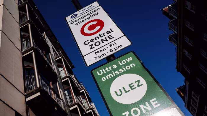 Signs for the Central London Congestion Charging Zone and Ultra Low Emission Zone stand on a street with buildings visible in the background.