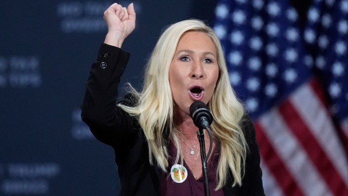 Rep. Marjorie Taylor Greene speaks at a podium with her fist raised, with American flags in the background.