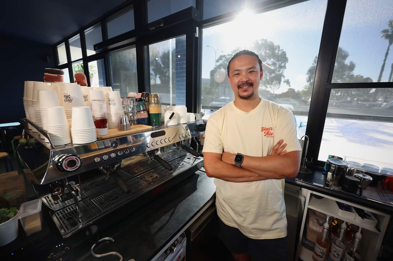 A cafe owner posing for a photo behind the counter and beside his coffee machine.
