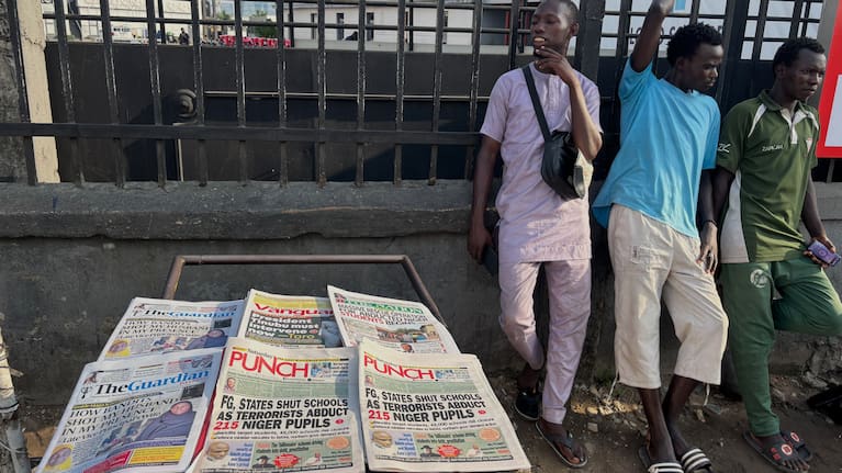 People stand near a display local newspapers on the street of Lagos with headlines on gunmen abducting schoolchildren and staff of the St. Mary's Catholic Primary and Secondary School.