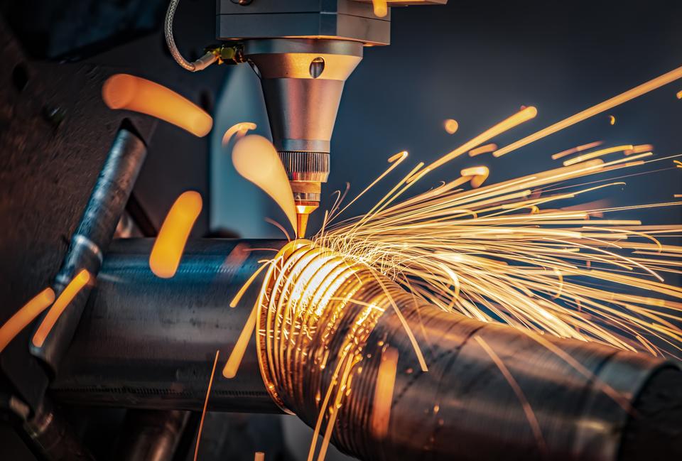 Sparks shoot off as a laser cutting head slices a metal pipe into thin circles.