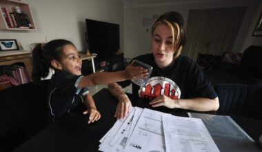 Mother and daughter at table, looking through documents of spending. Daughter handing phone to mum.