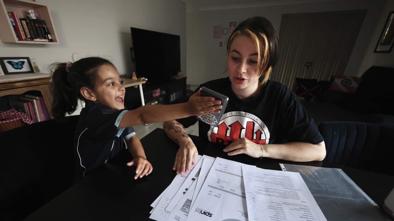 Mother and daughter at table, looking through documents of spending. Daughter handing phone to mum.