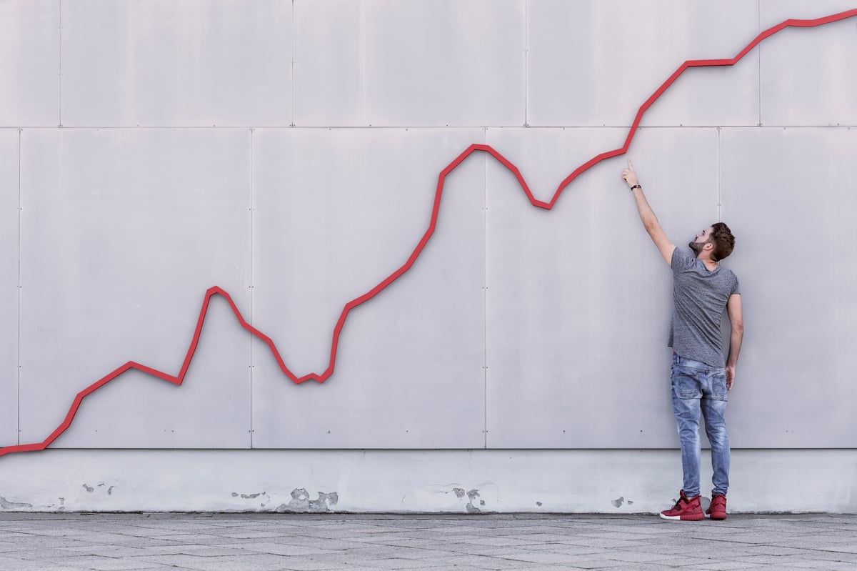 Person looking at a stock chart on a wall and pointing to it going up and to the right.