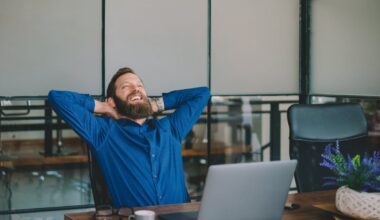 Professional leaning back in chair in office, smiling and relaxing at a desk with coffee and laptop.