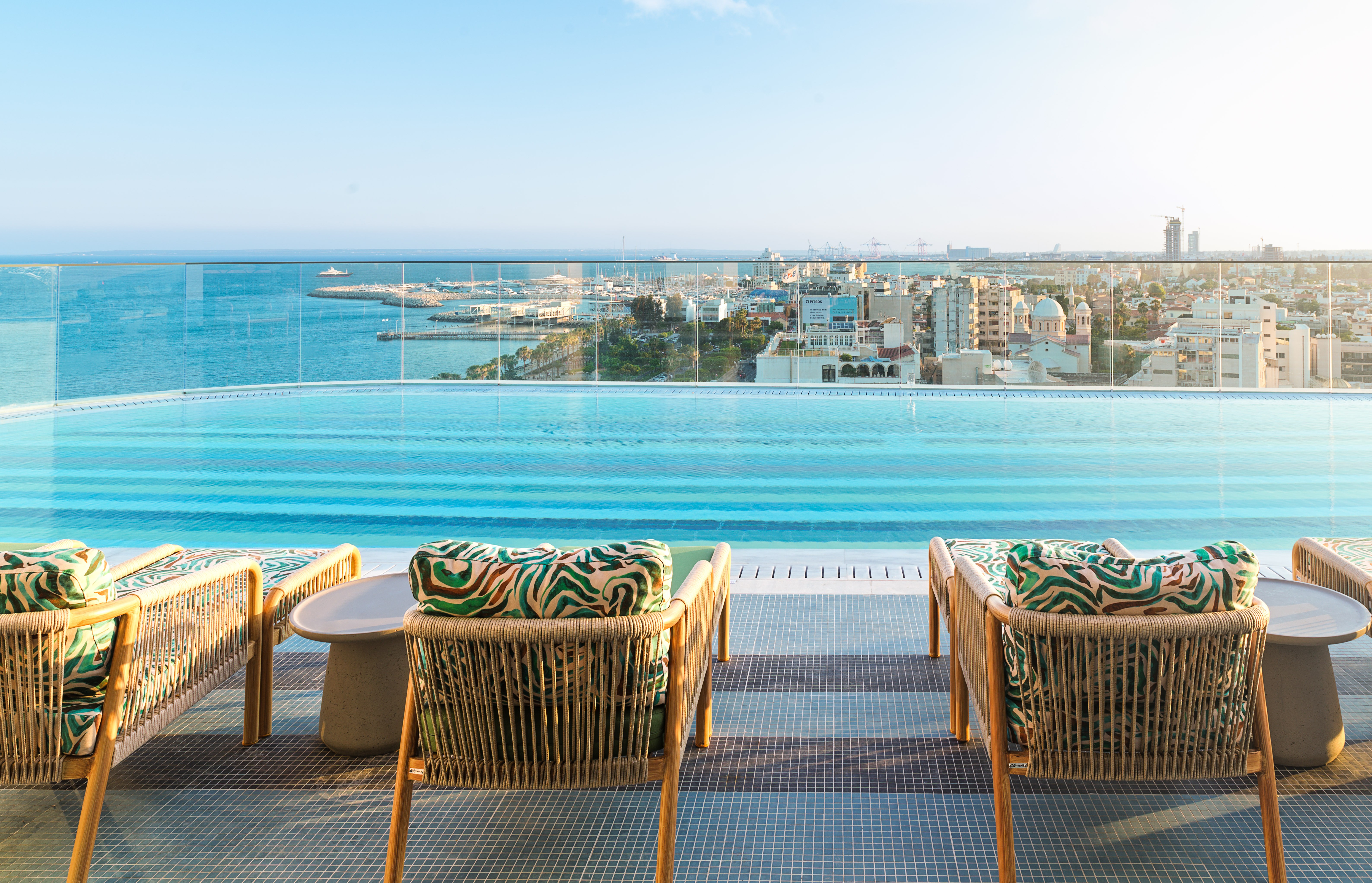 Rooftop infinity pool with lounge chairs overlooking Limassol city and the sea.
