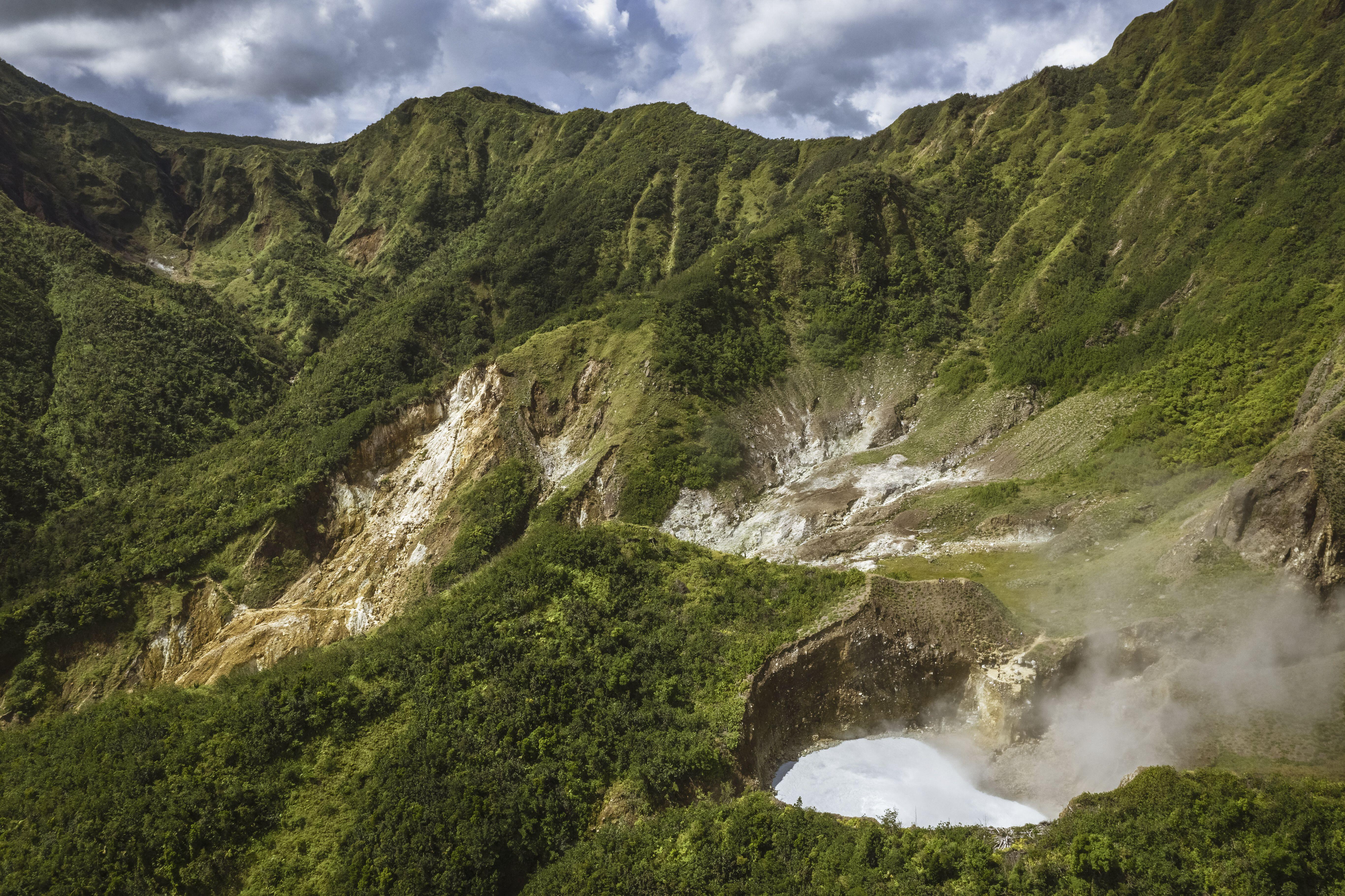 Aerial view of Dominica's Boiling Lake and Valley of Desolation in Morne Trois Pitons National Park, with lush green mountains and steaming fumaroles.