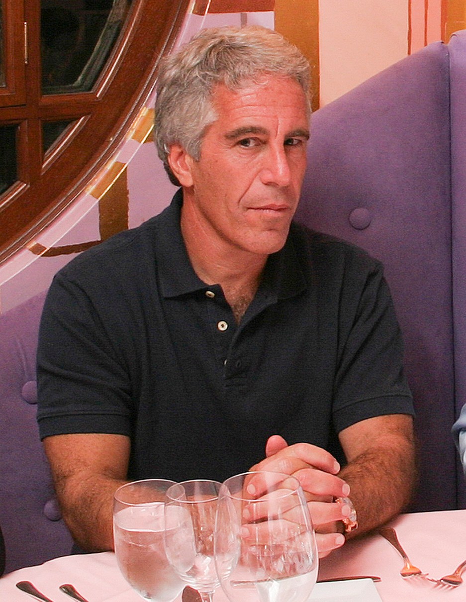 Jeffrey Epstein sitting at a table with hands clasped.