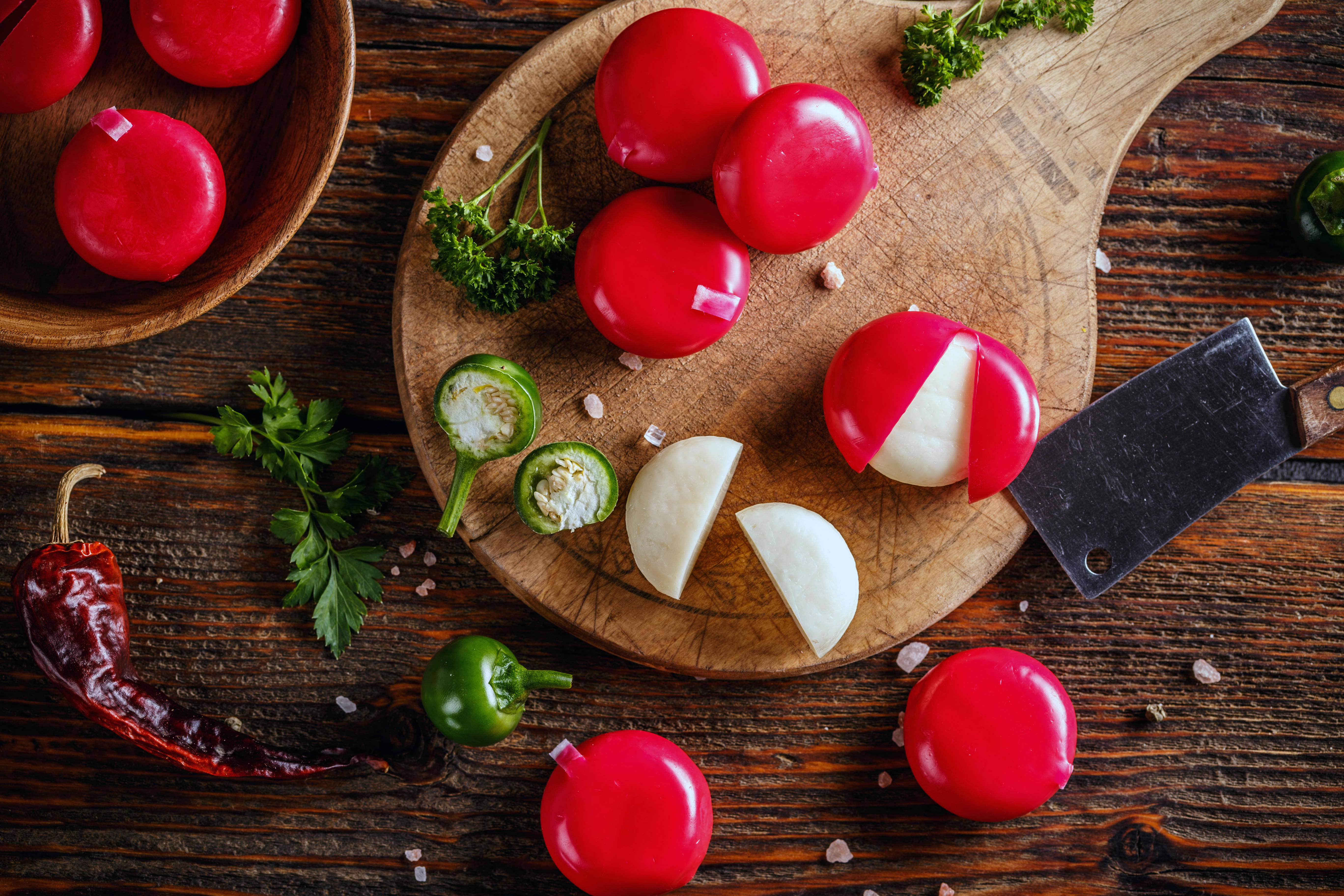 Top view of babybel cheese in red wax, some cut open on a wooden table with spices.