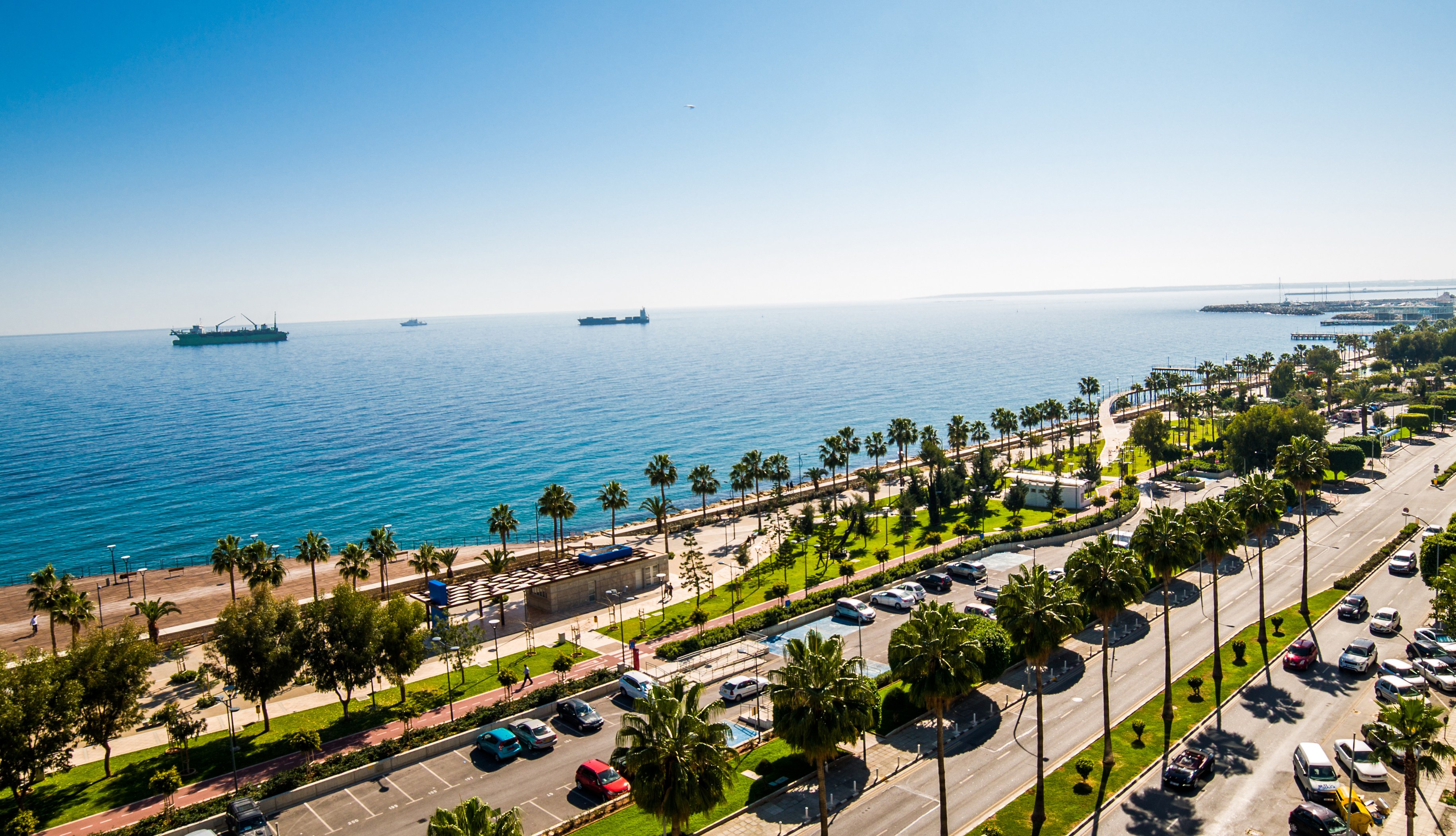 Aerial view of Limassol coastline with palm trees, a road with cars, and boats on the sea.