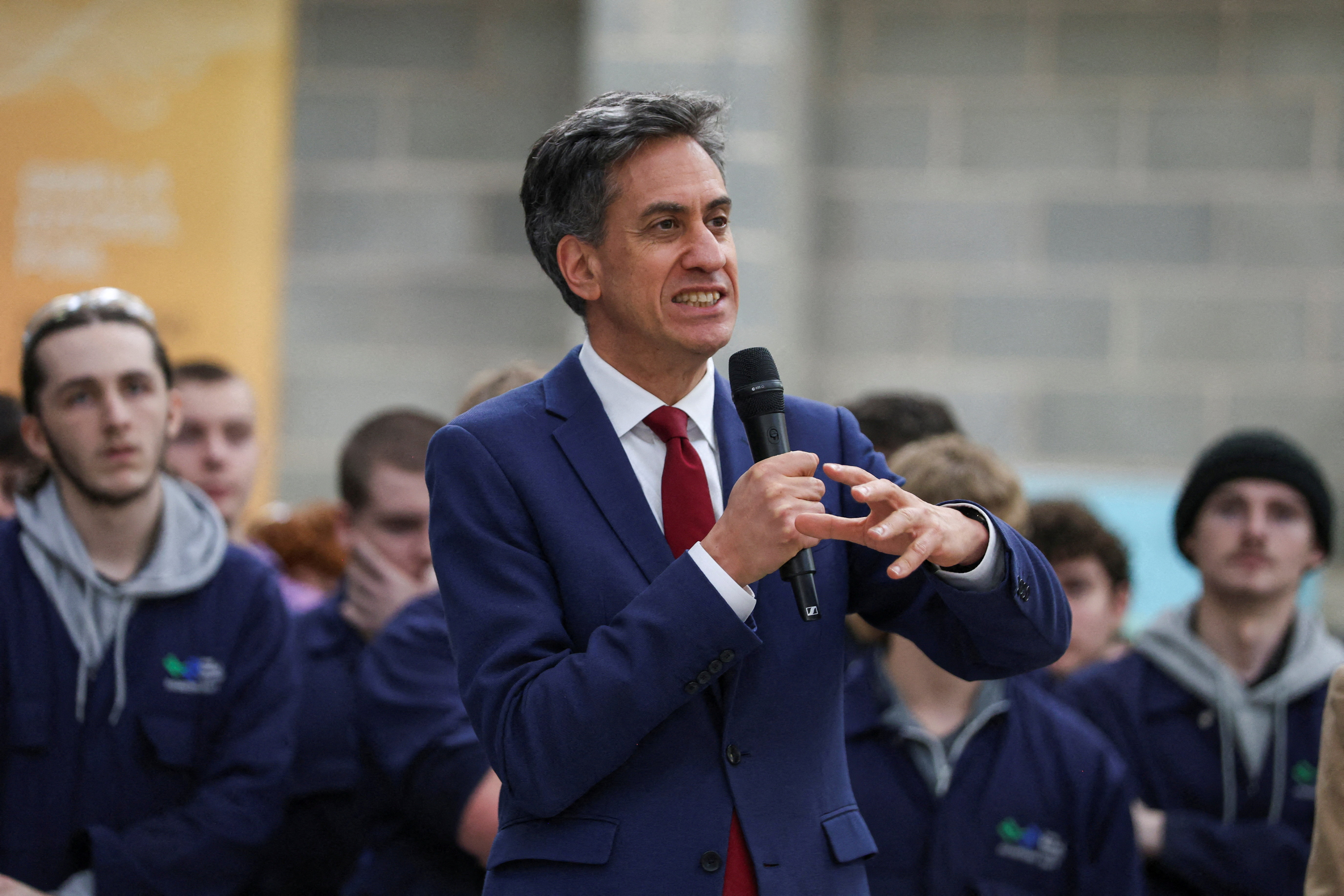 Britain's Secretary of State for Energy Security and Net Zero, Ed Miliband, speaking with a microphone while visiting Coleg Menai’s engineering workshop.