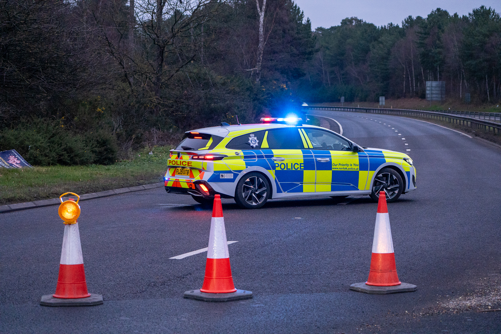 A Norfolk police car with flashing lights blocking a road with traffic cones.