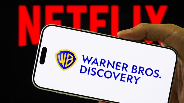CHONGQING, CHINA – DECEMBER 6: In this photo illustration, a smartphone displays the logo of Warner Bros. Discovery (NASDAQ: WBD) in front of a blurred red Netflix logo, on December 6, 2025, in Chongqing, China. Netflix has announced an agreement to acquire Warner Bros. Discovery in a deal valued at