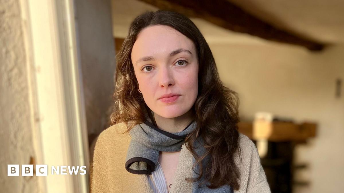 Amelia is standing in her doorway, with her empty front room behind her.