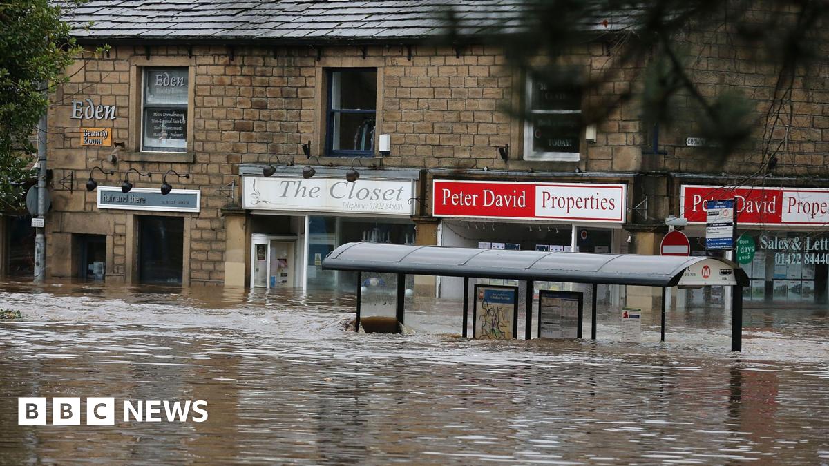 A bus stop and a row of shops under water in Hebden Bridge