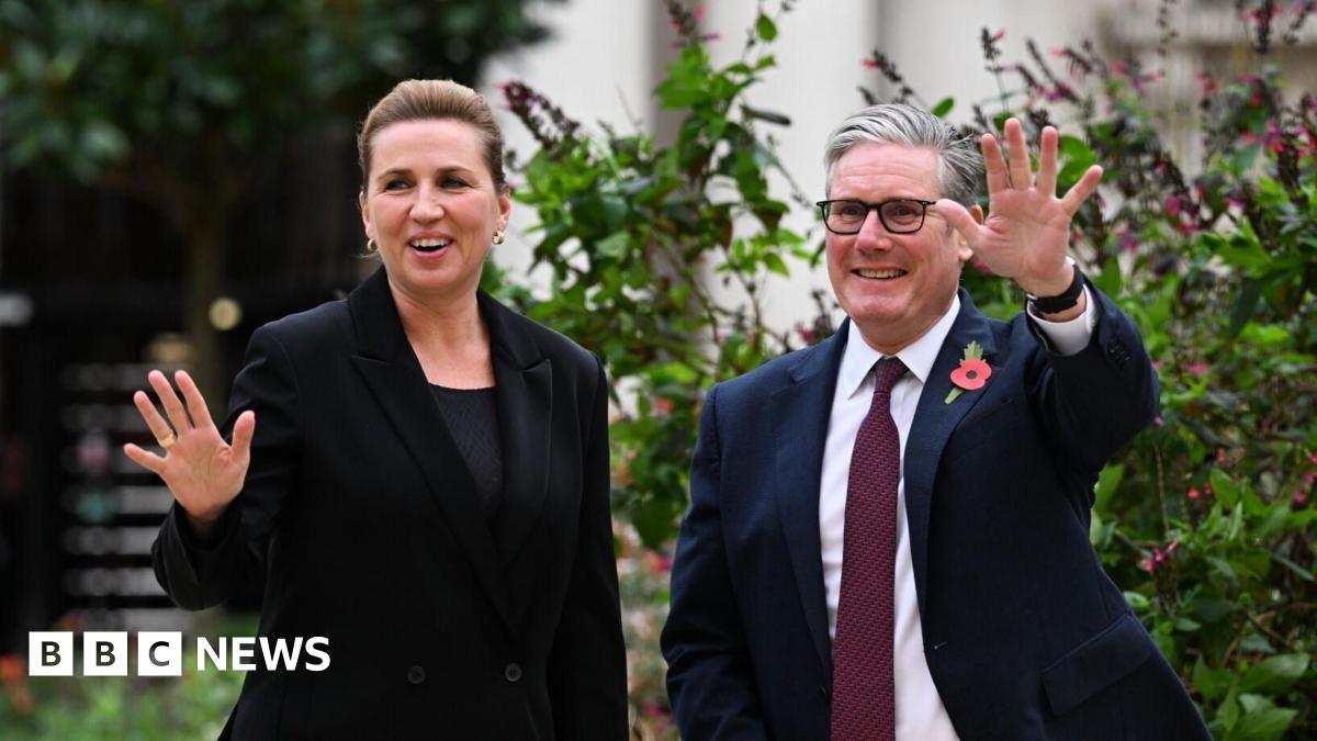 A brown NC500 sign post which says it is 27 miles to Ullapool next to a country road with hills in the background.