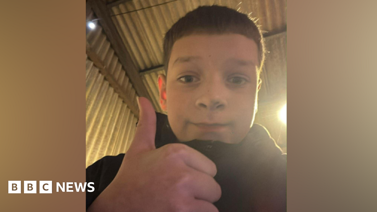 Aaron Anderson is wearing a zipped-up coat and is holding a thumbs up next to the camera. He is taking a selfie and smiling.