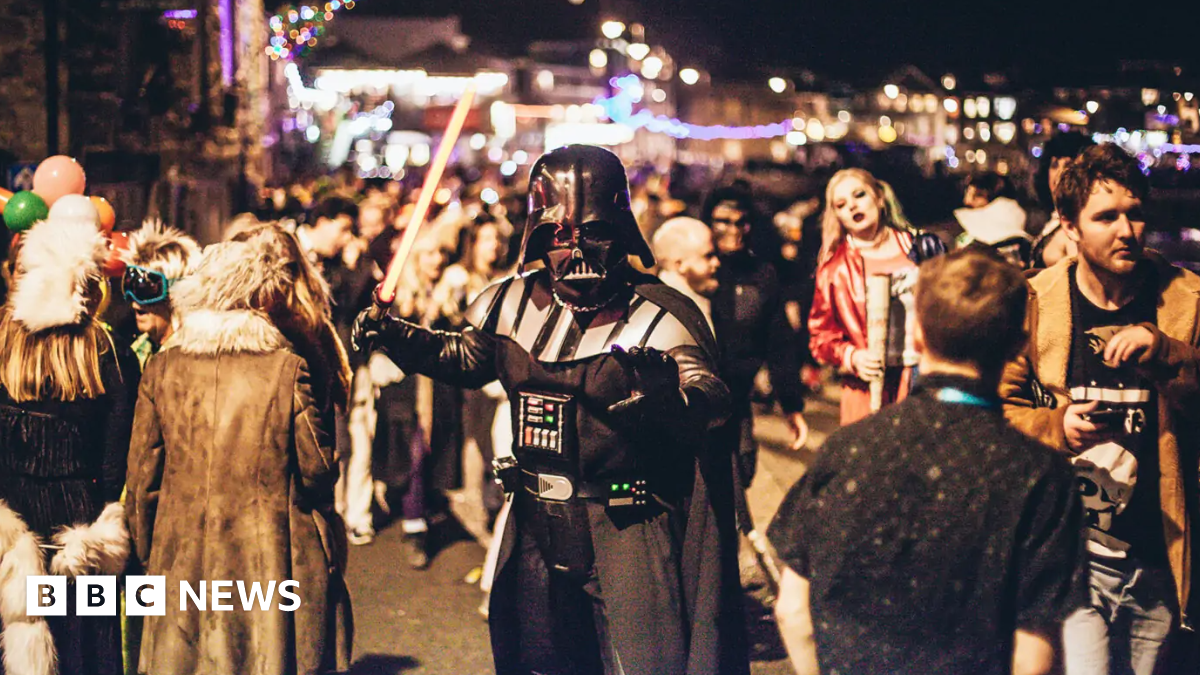 A person dressed as Darth Vader from Star Wars stands in a street full of people