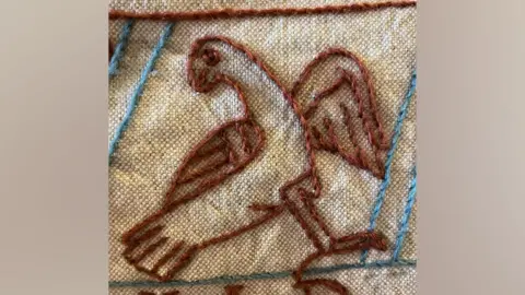 Mia Hansson Close-up of embroidery stitching of a bird standing at a slant, appearing not quite an accurate depiction 
