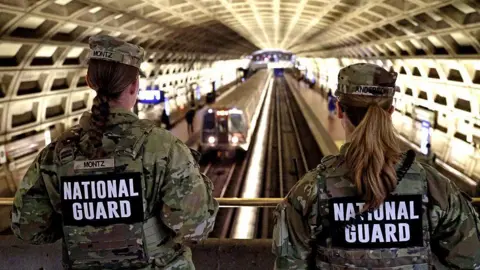 Getty Images view of the backs of two National Guard members in camo uniforms overlooking a train station in DC