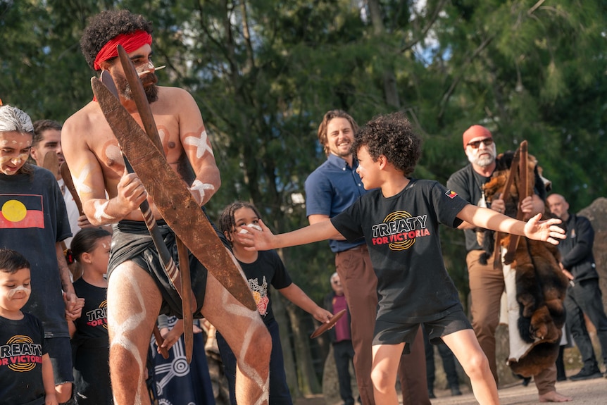 A group of people watch as a man in traditional Indigenous garb dances outdoors.