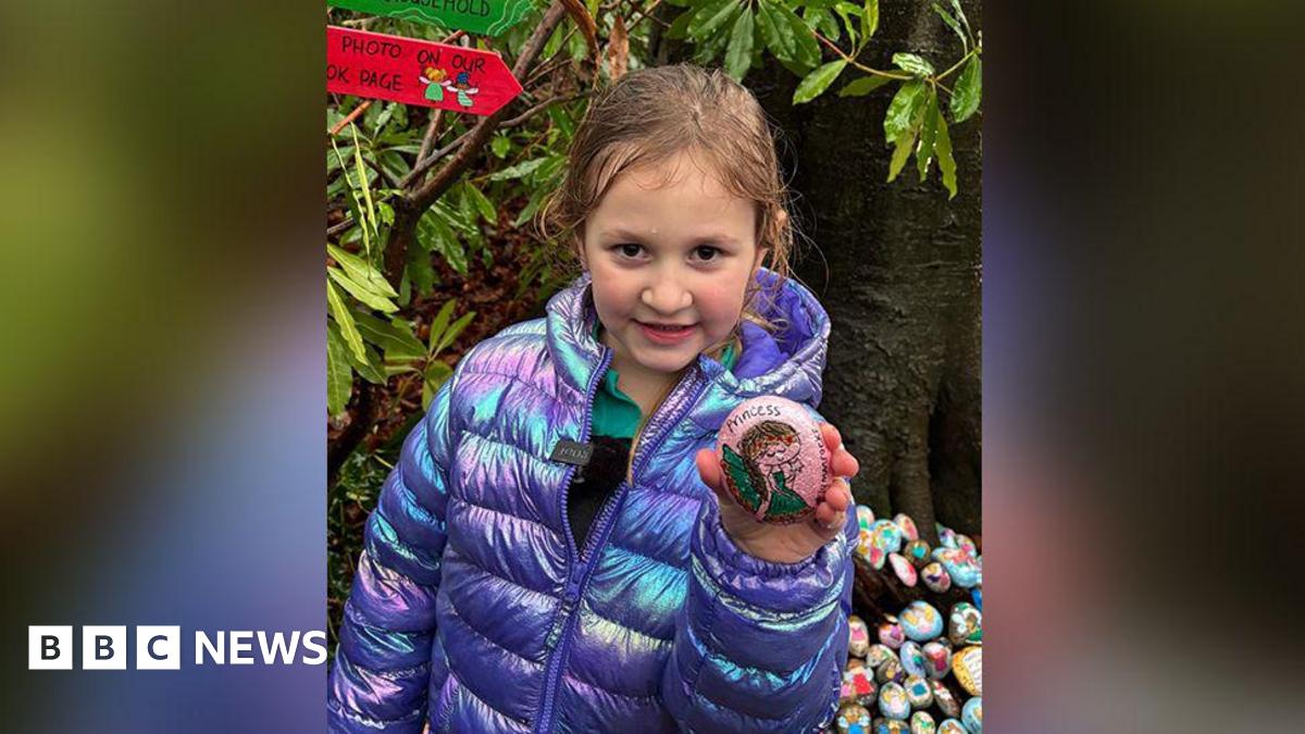 Beatrice, with brown hair and brown eyes, wears a luminous purple and pink coat while holding a rock featuring a painting of a princess.