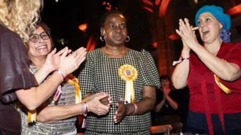 PA Media Nnena Kalu in the moments after the Turner Prize announcement, standing up with three supporters who are applauding and smiling