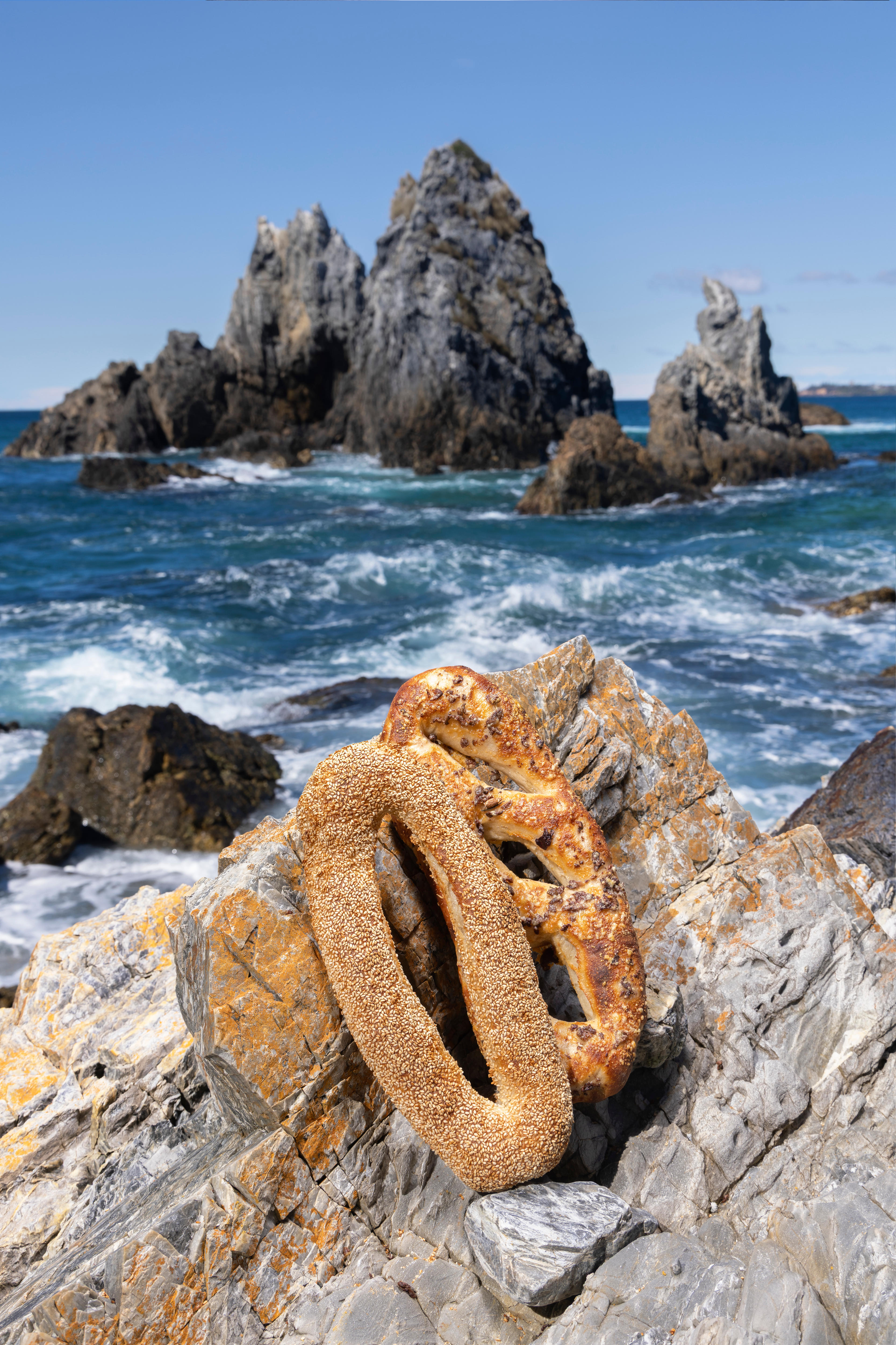 An oval shaped flatbread in front of a large rock protruding from the ocean.