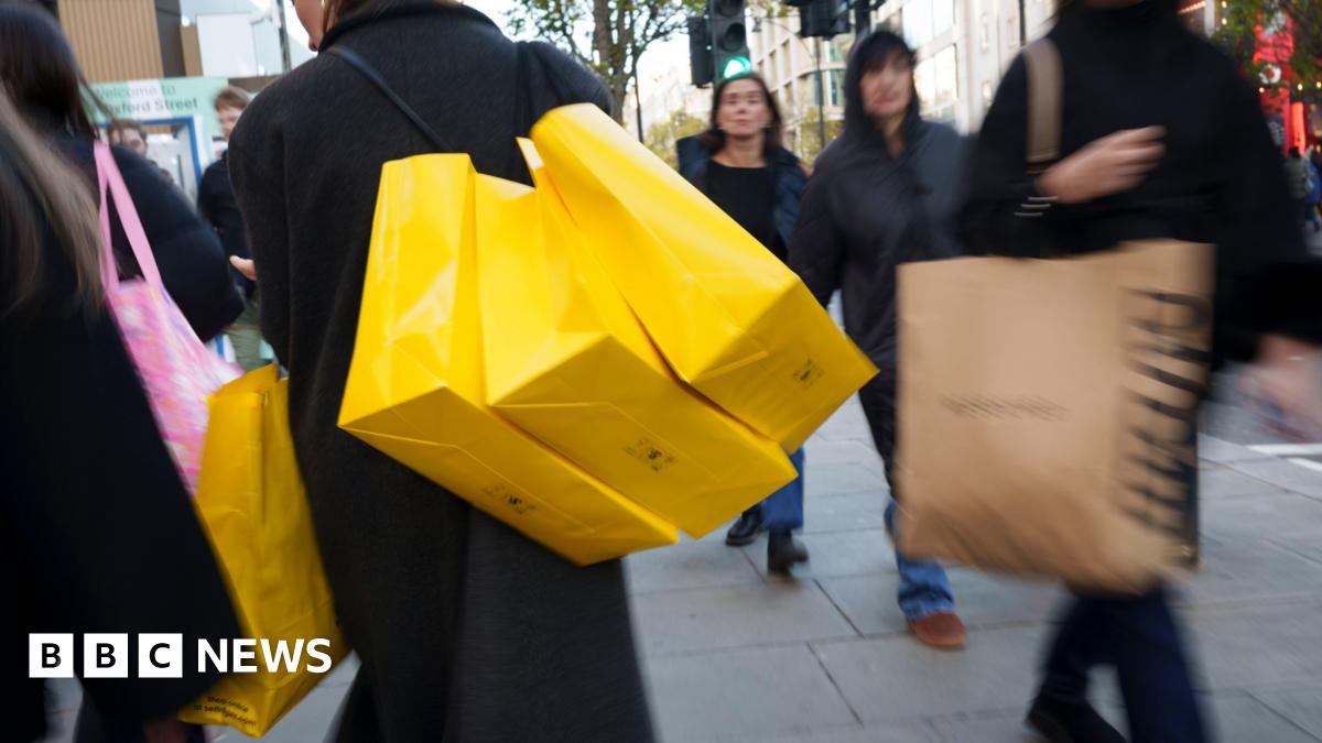 Shoppers dressed in woollen coats and puffer jackets walk with their bright yellow Selfridges shopping bags down Oxford St in London
