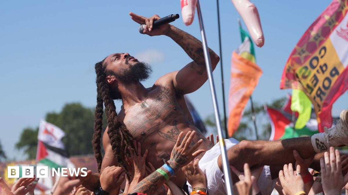 Bob Vylan crowd surfs during his performance at Glastonbury Festival. He is topless and is wearing white shorts and holding the mic in his left hand