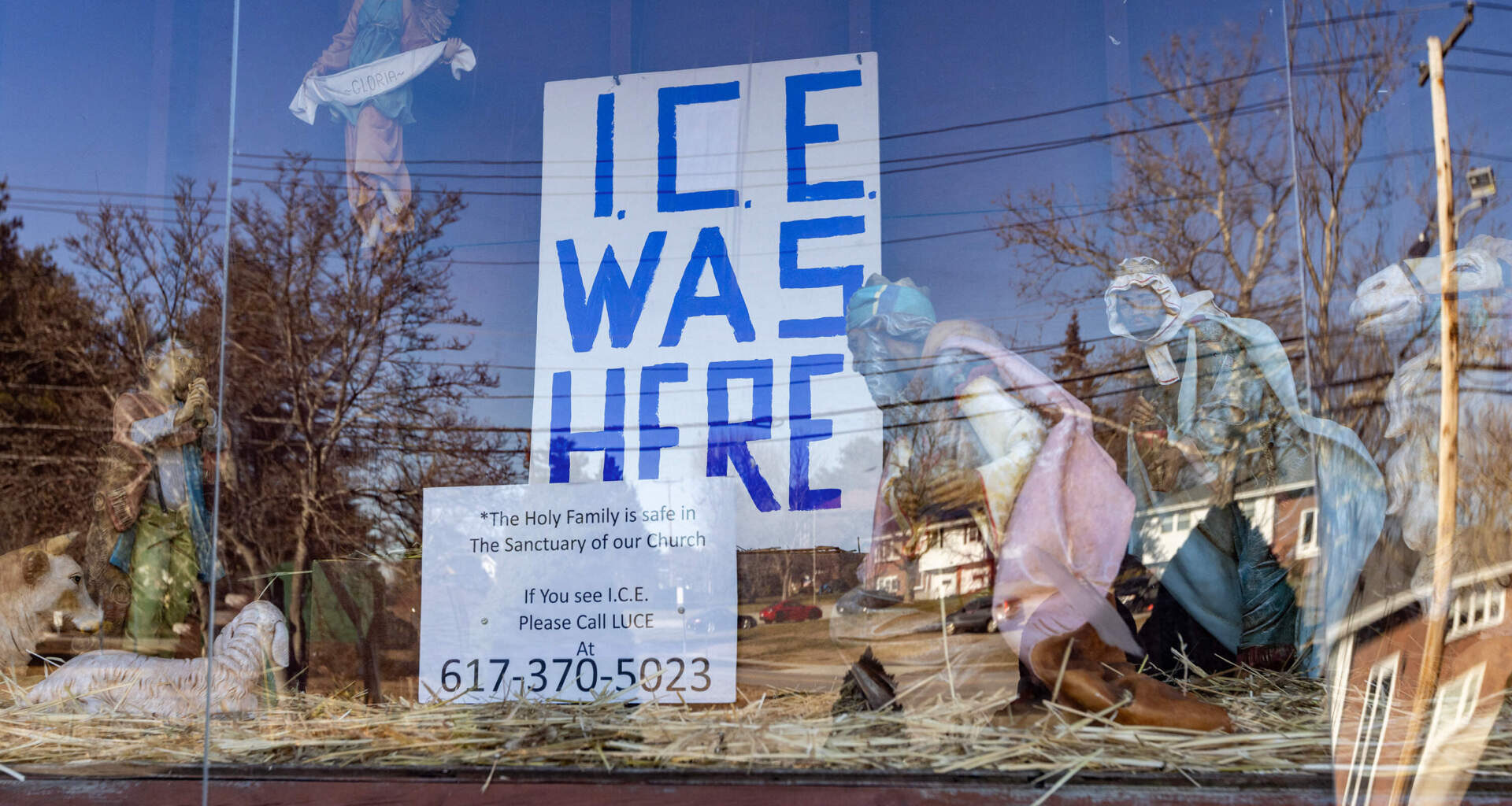 The annual nativity at St. Susanna’s Parish replaces the religious figurines with an “ICE Was Here” sign on Dec. 12. Below the display, reads another sign that says, “The Holy Family is safe in our Church ... If you see ICE please call LUCE at 617-370-5023.” (Jesse Costa/WBUR)