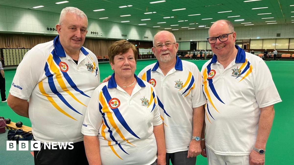 A group of four people wearing white bowls t-shirts in front of the green.