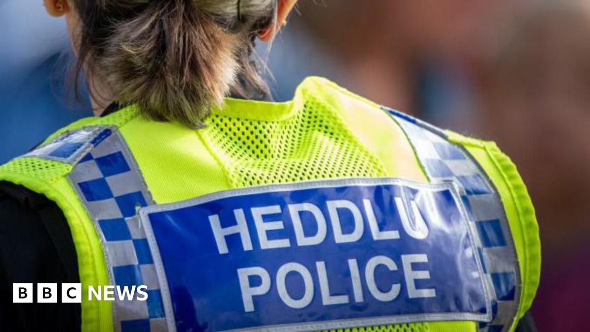 Police person with a neon vest that says Heddlu/Police. They have a ponytail and a black hat.