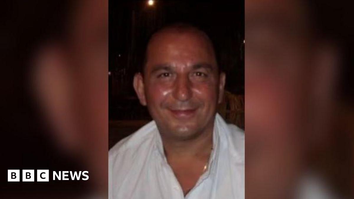 An image of Charlie Prodromou, a man with short dark hair wearing a white shirt and a gold chain, smiling at the camera