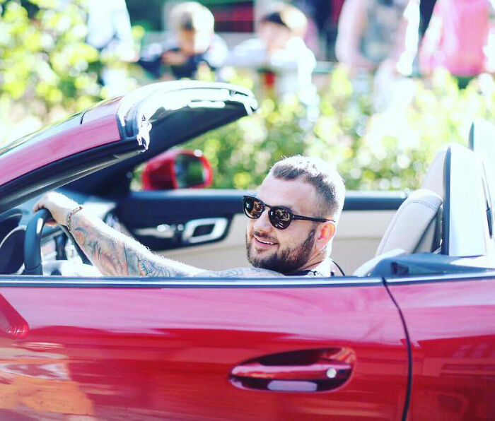 Man with sunglasses smiling while sitting in red convertible car, related to crypto scammer case news in Dubai.