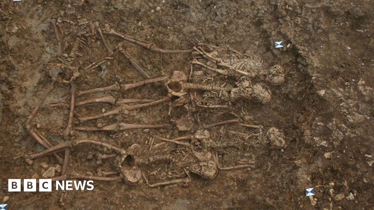 About five skeletons buried in the ground lying close to one another. There are markings in the corners which have probably been put there by archaeologists working on the site.