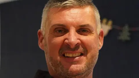 Andy Walpole Andy Walpole with short grey hair and stubble, smiling and looking at the camera.