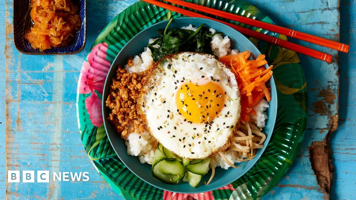 Bibimbap, a Korean dish featuring rice and various vegetables such as carrots, spinach, bean sprouts and a fried egg on top, served with chopsticks, and a side dish of kimchi.