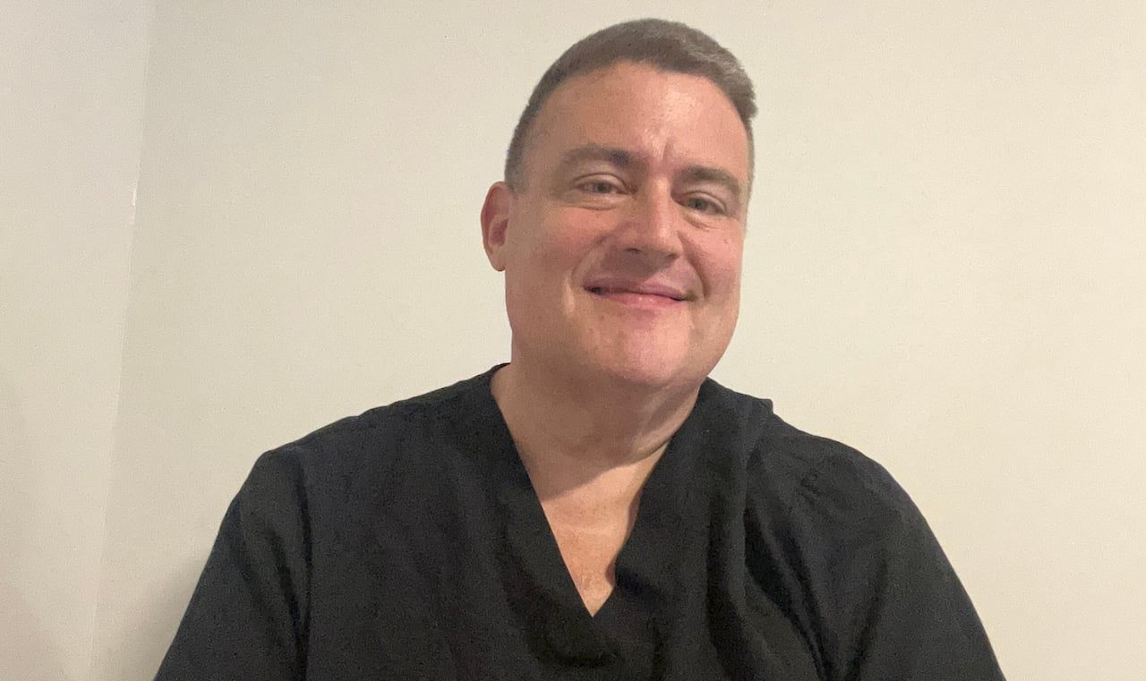 A man in black scrubs looks at the camera.