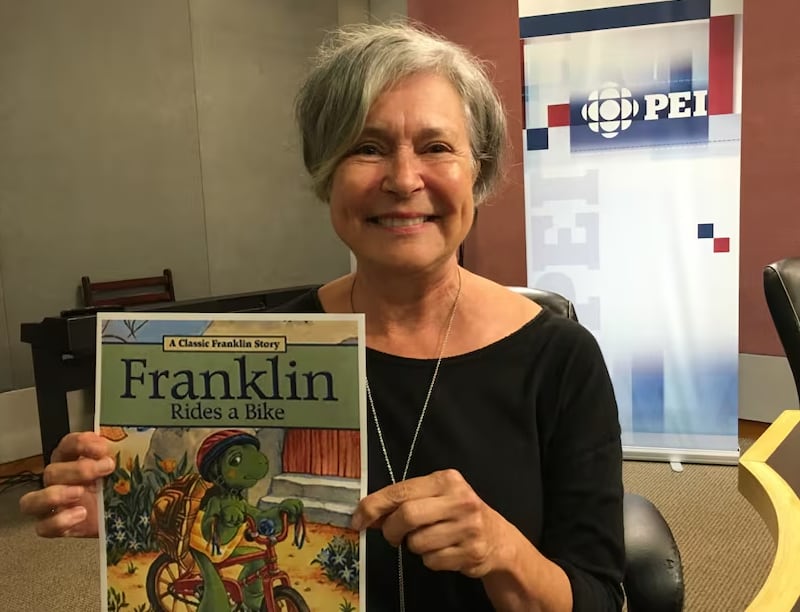 A woman holds up a book that says Franklin Rides  a Bike
