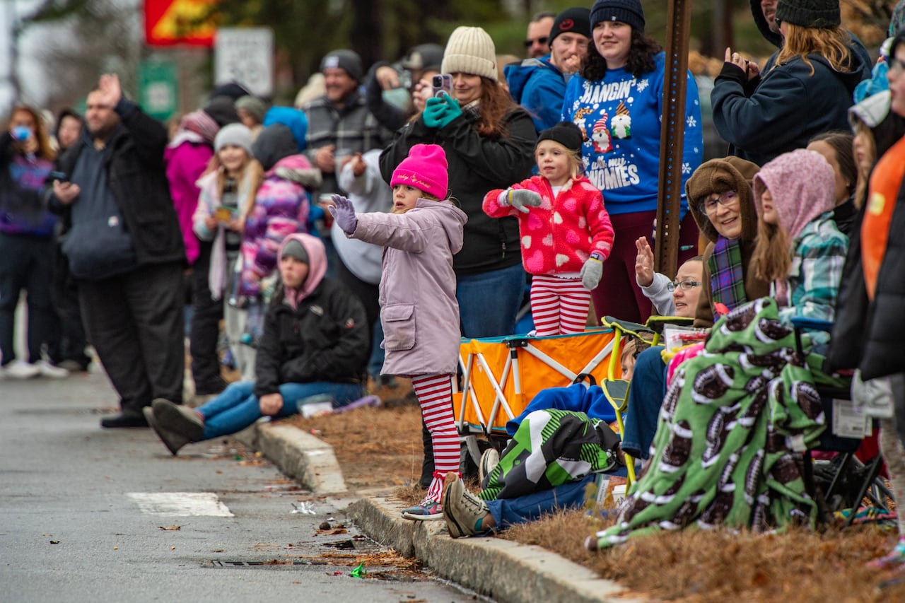 A crowd of children stands on a sidewalk for a parade