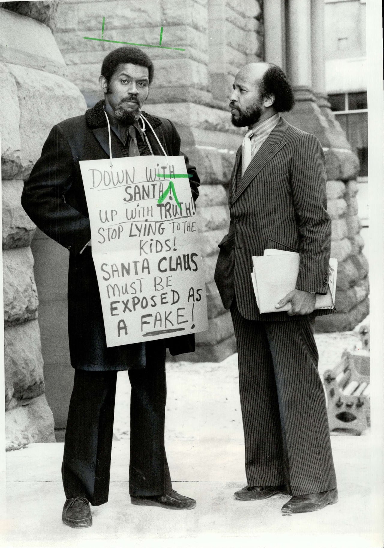 A black and white photo shows a man wearing a sign that says down with Santa, Sant Claus must be exposed