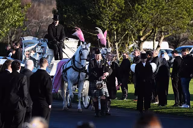 A piper plays while leading a white horse-drawn hearse