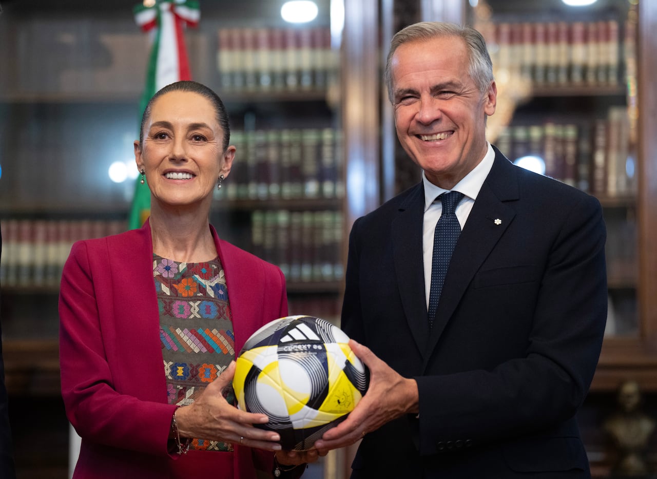 A man and a woman hold a yellow, black and white soccer ball and pose for a photo in front of a wall of books. 